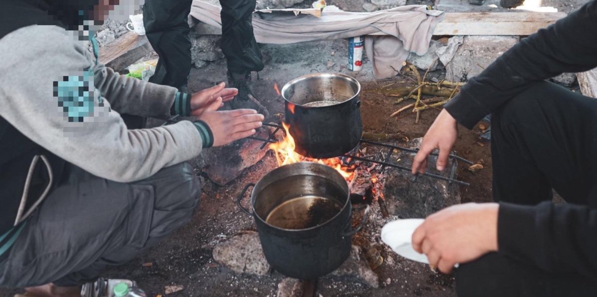 Food provisions - Three refugees heating pots of water over an open fire; the photo is cropped so their faces are not shown