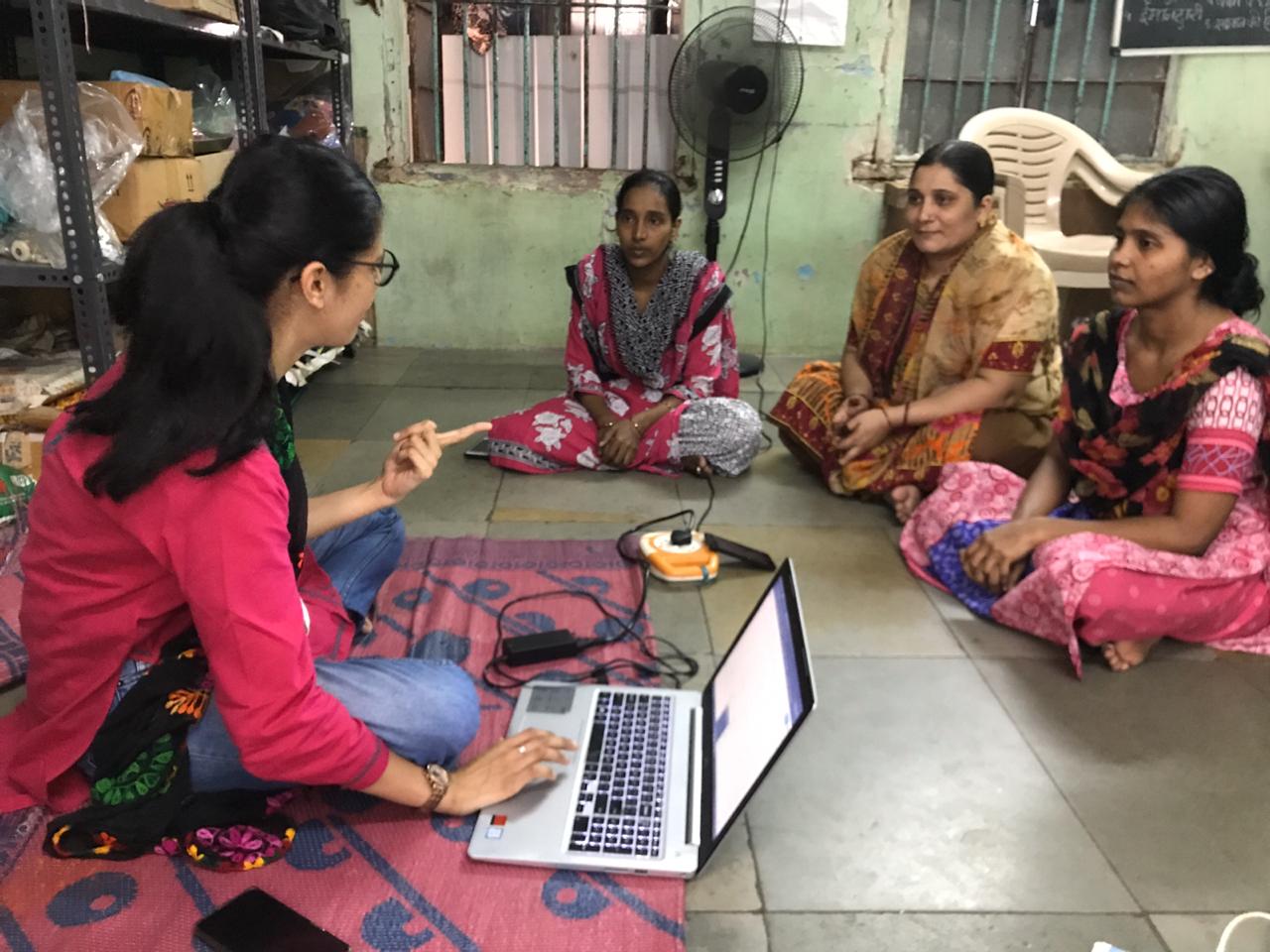 Social change a woman sitting on the floor indoors uses a computer and microphone as she talks with three other sitting women