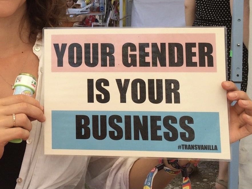 A transgender flag reading "Your gender is your business" held by a pair of hands