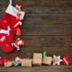 A red ans white Christmas stocking hanging abovean assortment of handmade christmas tree ornaments and gift boxes, set against darl wood paneling