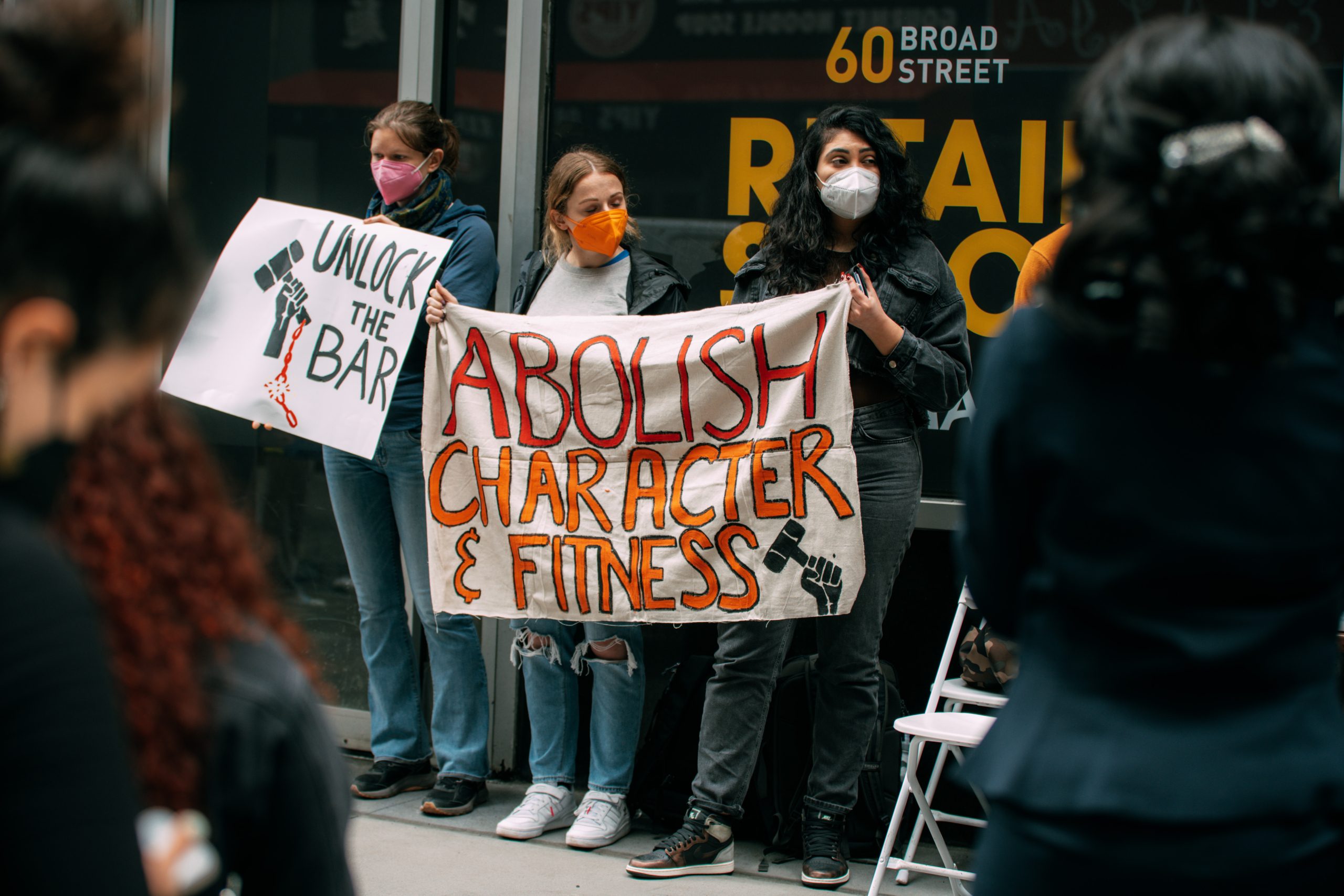 Three people on a sidewalk at a FILSAA event holding hand-painted banners, one reading Unlock the Bar and the other reading Abolish Character & Fitness