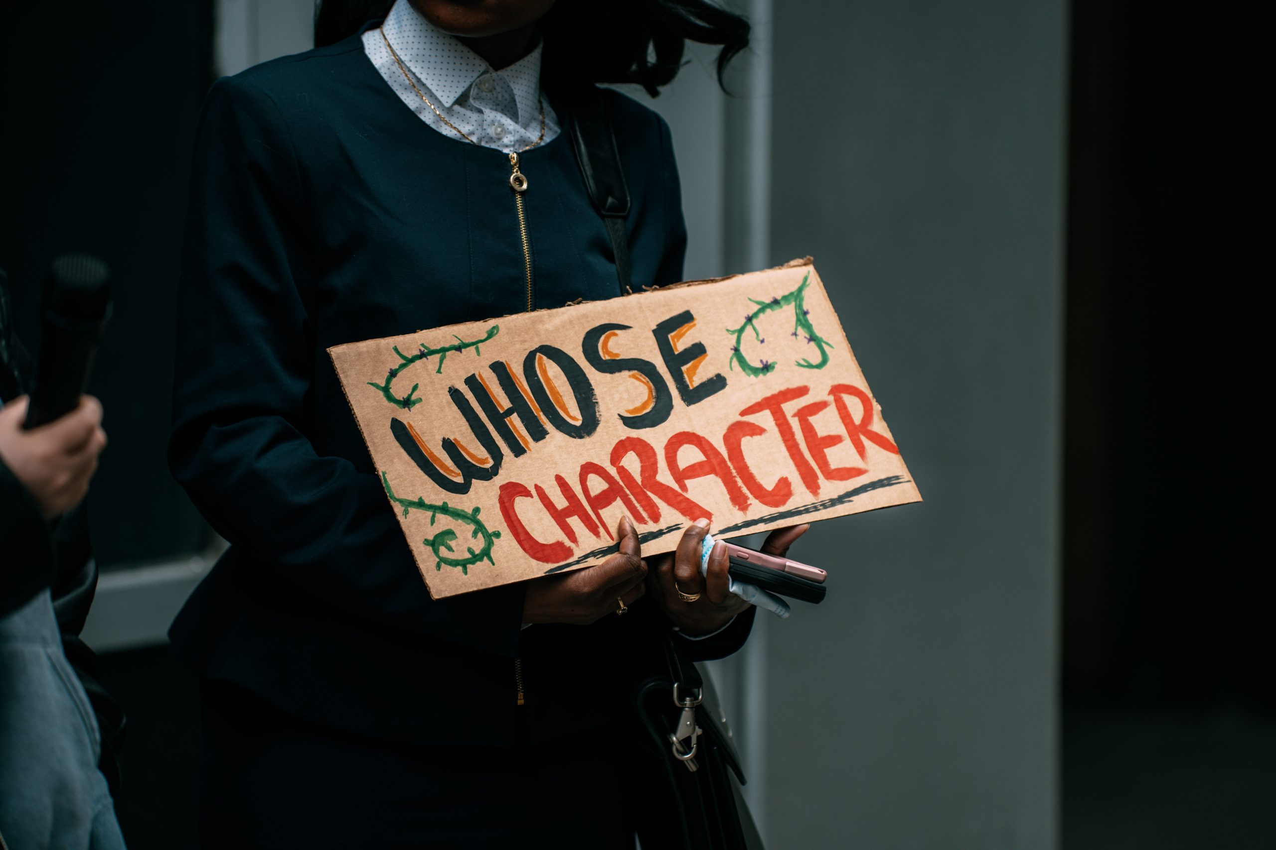 Person from FILSAA holding a hand-painted cardboard that reads "Whose Character"